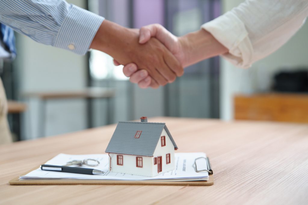 A handshake over a real estate contract and a model house representing a successful home selling process