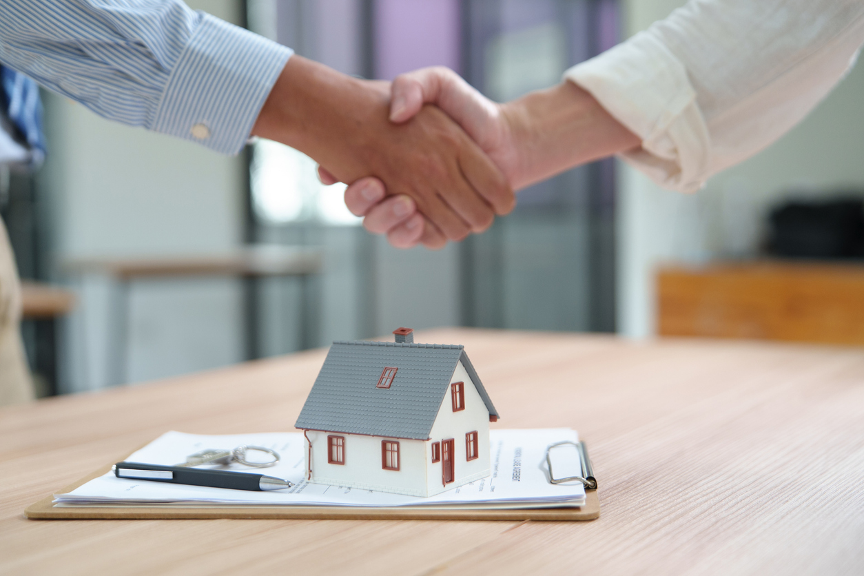 A handshake over a real estate contract and a model house representing a successful home selling process