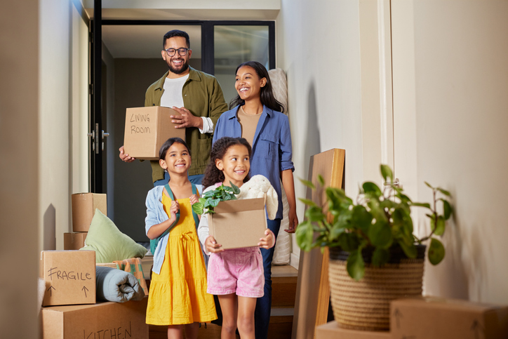 A happy, smiling family walking into their new home with boxes, experiencing a stress-free transition when moving to a new city with a trusted real estate agent.